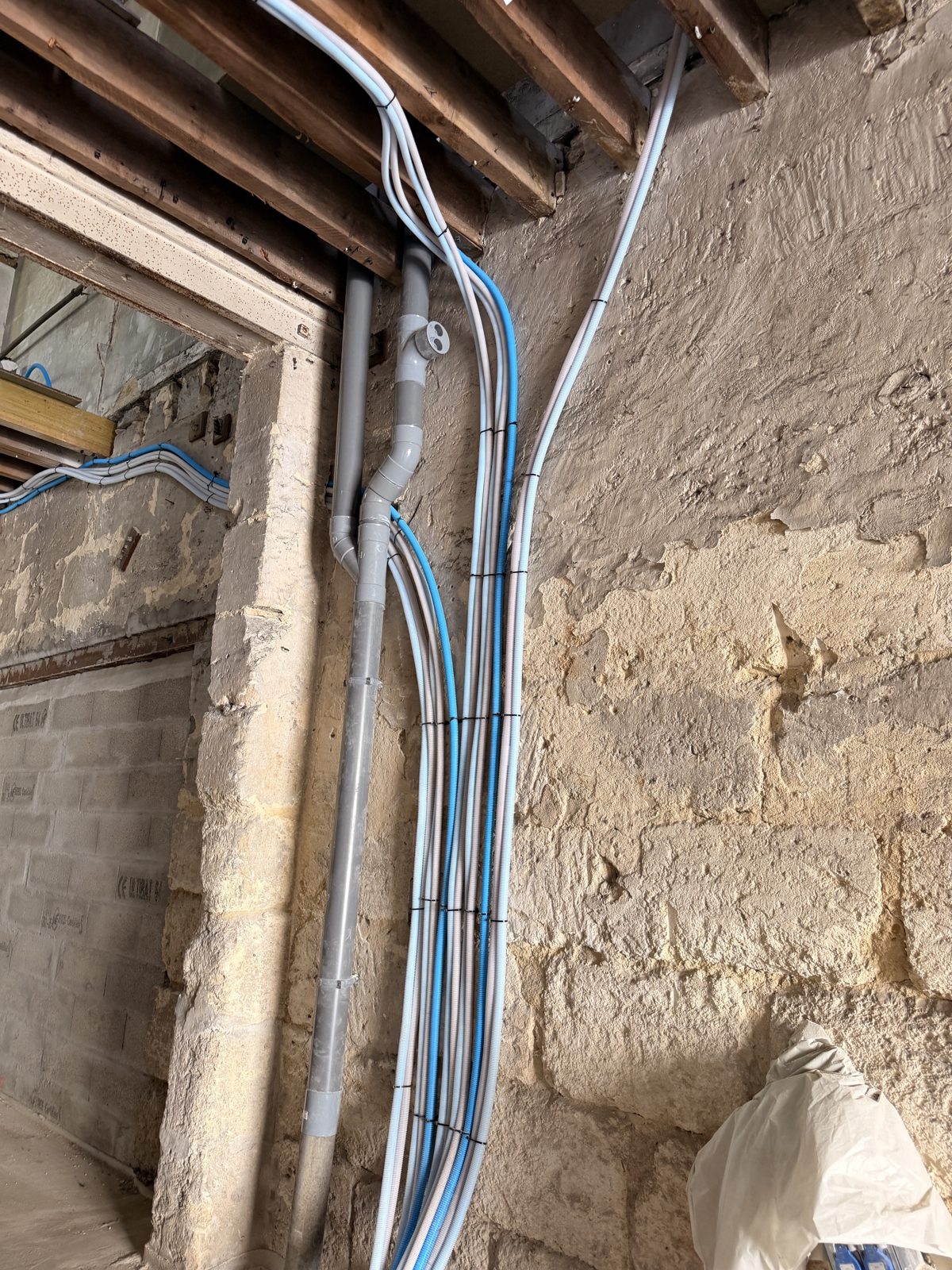 Réseaux d'évacuation PVC et gaines électriques posés sur un mur en pierre